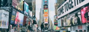Times Square skyline filled with colorful digital billboards, including one with bold text that reads “COME TOGETHER.”