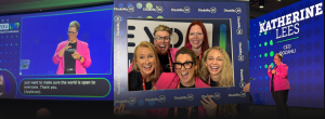 A 3-photo collage. From left to right: Katherine in pink blazer on the screen with the caption "just want to make sure the world is open to everyone. Thank You. (applause)", a team of 5 women holding a frame that has Disability:IN logo all around and smiling toward the camera, Katherine in the pink blazer standing on stage with the background screen showing her name and role, "Katherine Lees, CEO, dozanu".